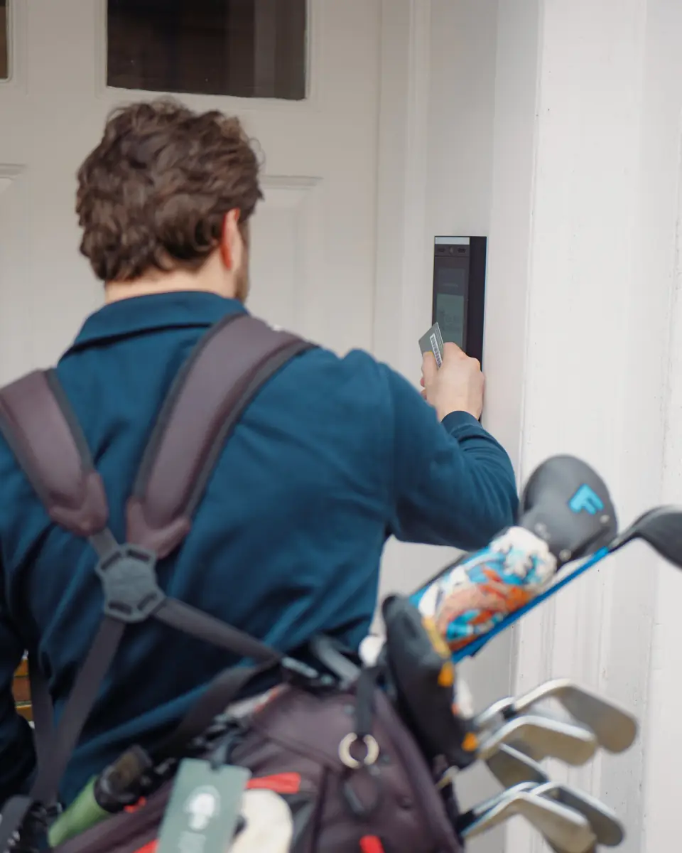 Man with a golf bag on his back paying at a door with a card reader.